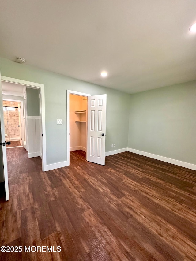 unfurnished bedroom featuring recessed lighting, baseboards, dark wood finished floors, and a spacious closet