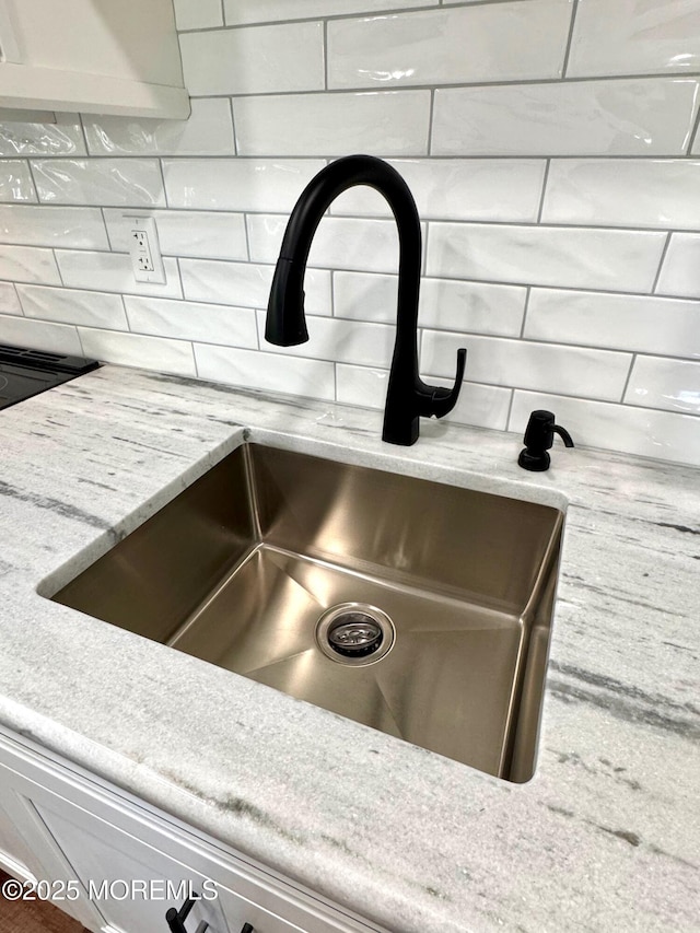 interior details featuring a sink, tasteful backsplash, and light stone countertops