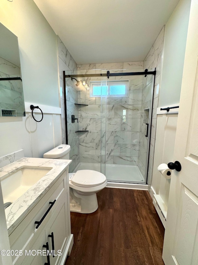 bathroom featuring vanity, toilet, a marble finish shower, wood finished floors, and a baseboard radiator