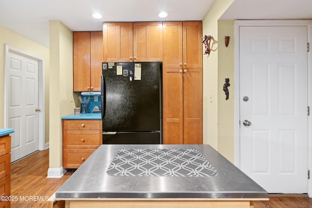 kitchen with freestanding refrigerator, stainless steel countertops, wood finished floors, recessed lighting, and baseboards