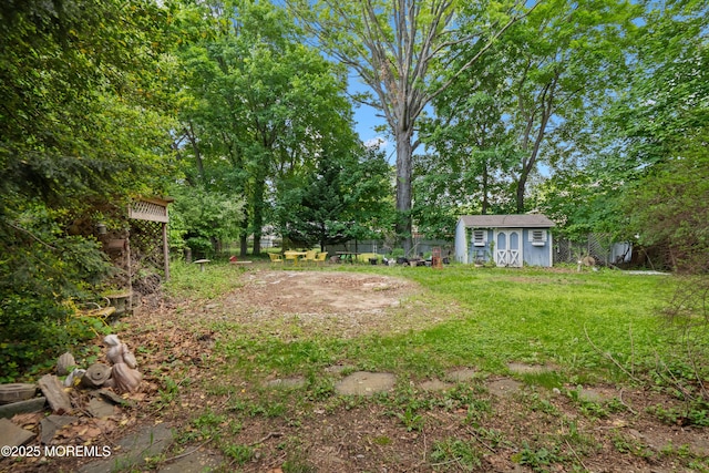 view of yard with a storage shed, an outbuilding, fence, and view of wooded area