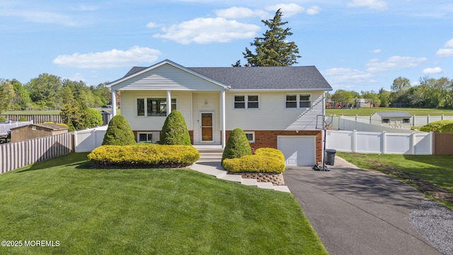 raised ranch with a garage, fence, a front lawn, and aphalt driveway