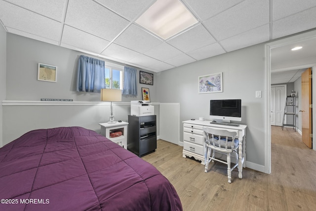 bedroom featuring baseboards, a paneled ceiling, and light wood-type flooring