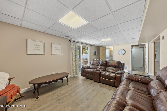 living room with light wood-style floors, baseboards, a drop ceiling, and visible vents