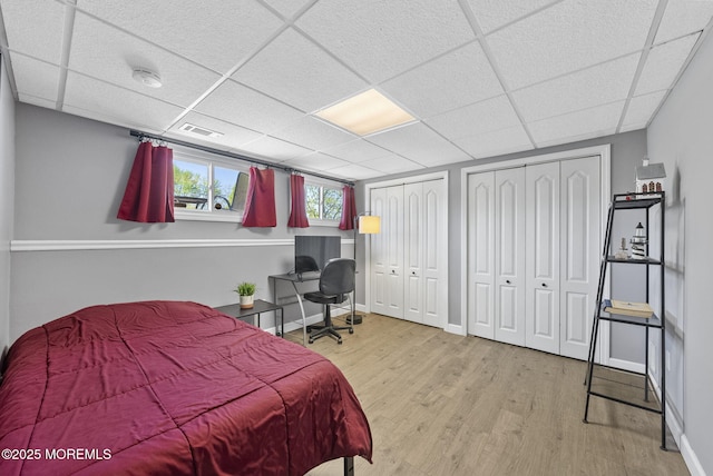 bedroom with multiple closets, baseboards, a drop ceiling, wood finished floors, and visible vents