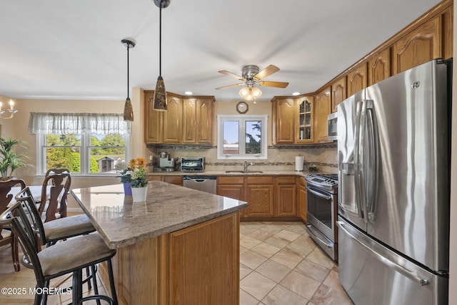 kitchen featuring decorative backsplash, brown cabinetry, a sink, stainless steel appliances, and a wealth of natural light