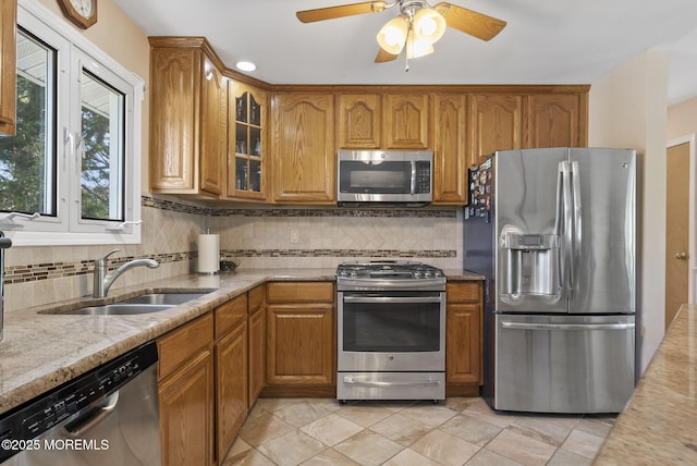 kitchen featuring a sink, brown cabinetry, stainless steel appliances, tasteful backsplash, and glass insert cabinets