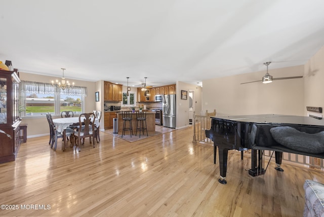 living area with baseboards, ceiling fan with notable chandelier, and light wood-type flooring