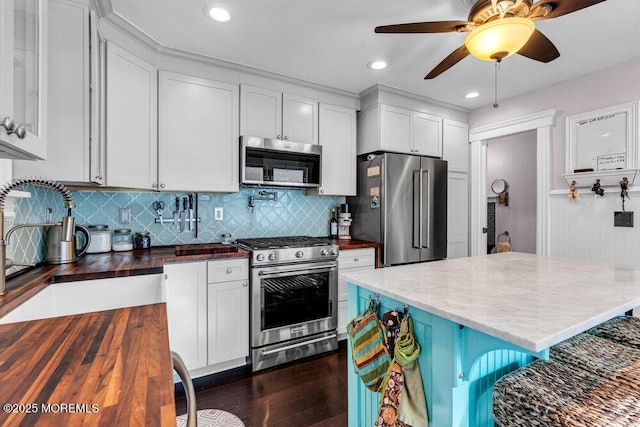 kitchen with ceiling fan, a sink, wooden counters, stainless steel appliances, and decorative backsplash