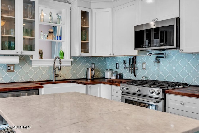 kitchen with appliances with stainless steel finishes, tasteful backsplash, a sink, white cabinets, and butcher block counters