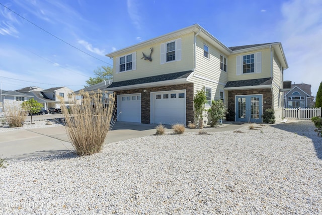 view of front of house featuring fence, stone siding, french doors, an attached garage, and driveway
