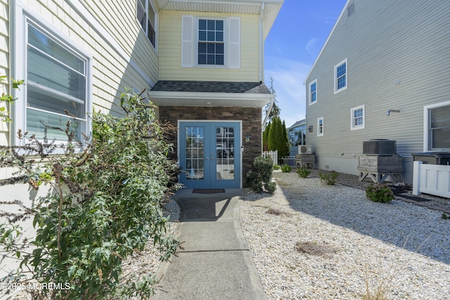 entrance to property featuring french doors, central AC, and roof with shingles