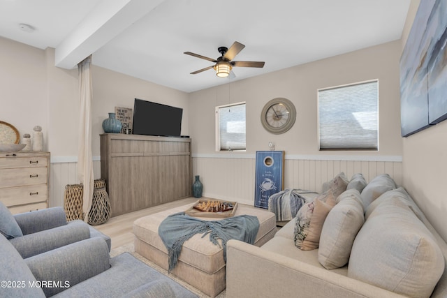 living area featuring a ceiling fan, wainscoting, and wood finished floors