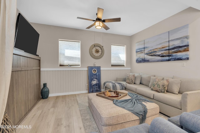 living area with a wainscoted wall, ceiling fan, and light wood finished floors