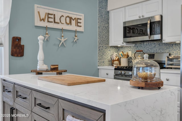 kitchen with decorative backsplash, appliances with stainless steel finishes, light stone countertops, a toaster, and white cabinetry