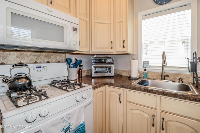 kitchen with a sink, dark countertops, cream cabinets, and white appliances
