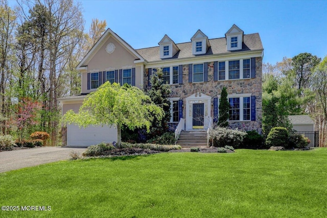 colonial-style house featuring an attached garage, a front lawn, stone siding, stucco siding, and driveway