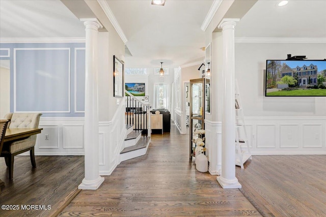 corridor featuring stairs, wood finished floors, ornamental molding, a decorative wall, and ornate columns