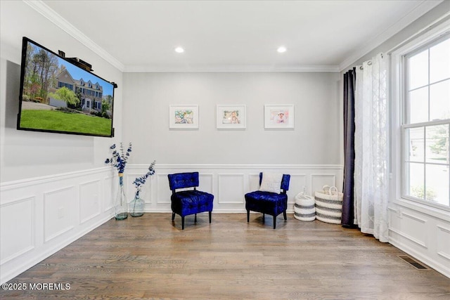 living area with crown molding, recessed lighting, wood finished floors, and a decorative wall
