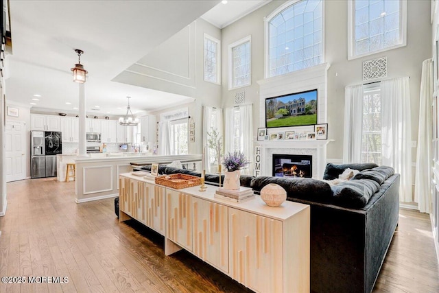 living room featuring a large fireplace, wood finished floors, ornamental molding, an inviting chandelier, and a high ceiling