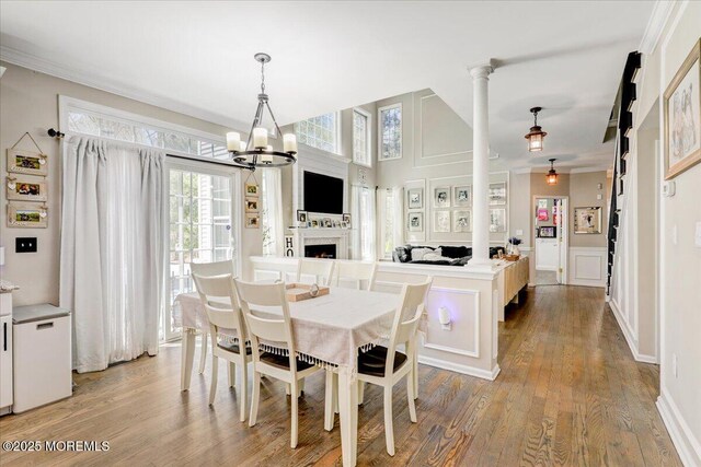 dining space with crown molding, a notable chandelier, a fireplace, a decorative wall, and light wood-style flooring