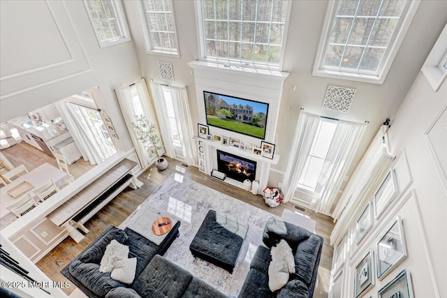 living room with a towering ceiling, wood finished floors, and a large fireplace