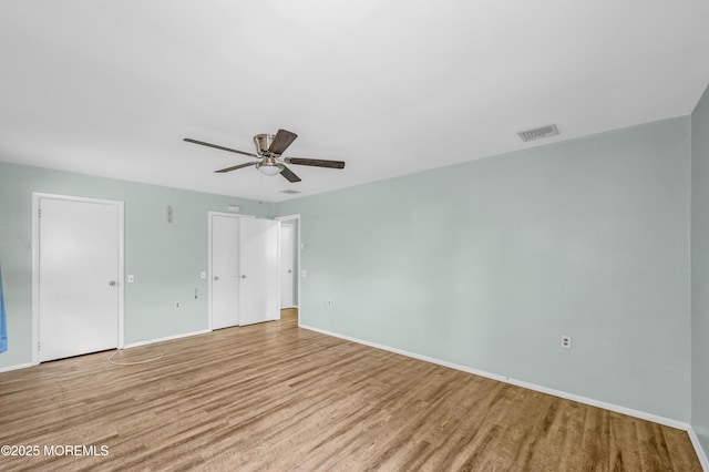unfurnished bedroom with wood finished floors, baseboards, two closets, and a ceiling fan