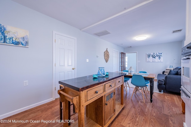 kitchen with brown cabinets, dark countertops, visible vents, and wood finished floors
