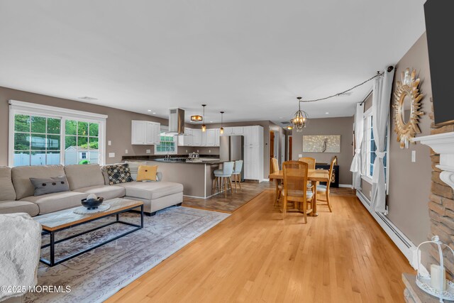 living room with a baseboard heating unit, a chandelier, and light wood-style floors