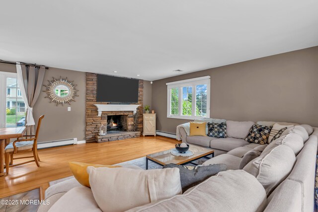 living room featuring a baseboard heating unit, wood finished floors, a stone fireplace, and baseboards