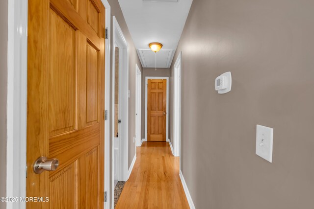 hall featuring attic access, light wood finished floors, and baseboards