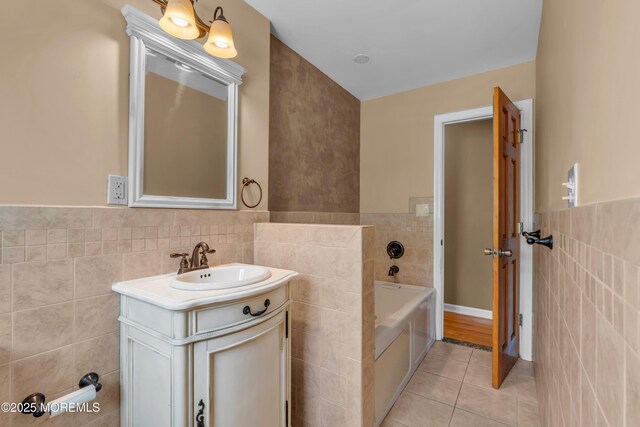 bathroom with tile walls, tile patterned floors, a wainscoted wall, vanity, and a bath