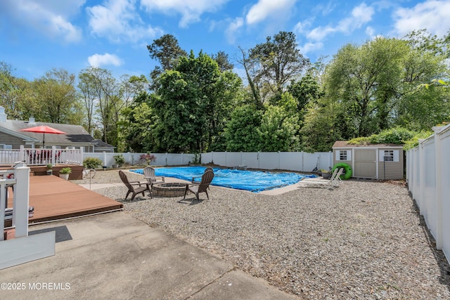 view of swimming pool featuring a deck, a fenced backyard, a shed, an outdoor fire pit, and an outdoor structure