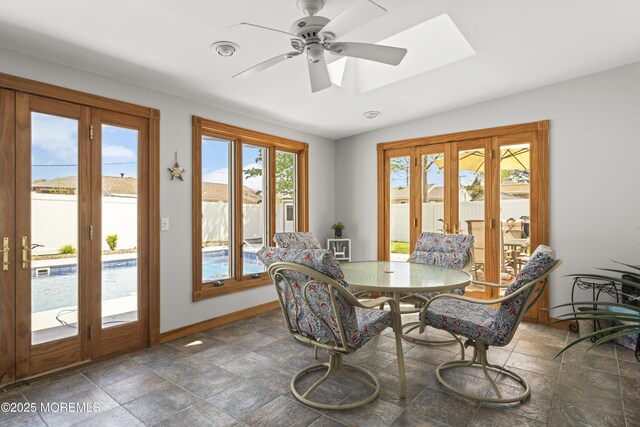dining space featuring a ceiling fan, a skylight, stone finish floor, and baseboards