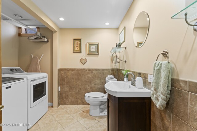 bathroom featuring tile walls, tile patterned flooring, wainscoting, toilet, and washer and clothes dryer