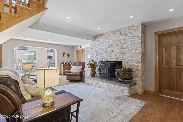 living room with a wood stove, wood finished floors, baseboards, recessed lighting, and arched walkways