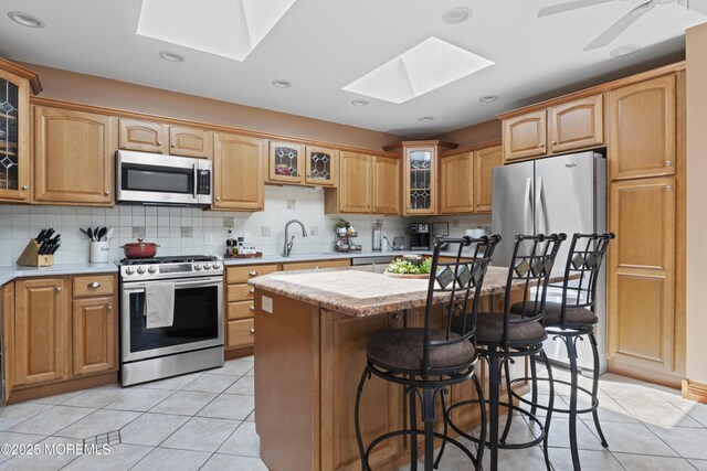 kitchen with a kitchen island, a kitchen bar, a skylight, appliances with stainless steel finishes, and light tile patterned floors