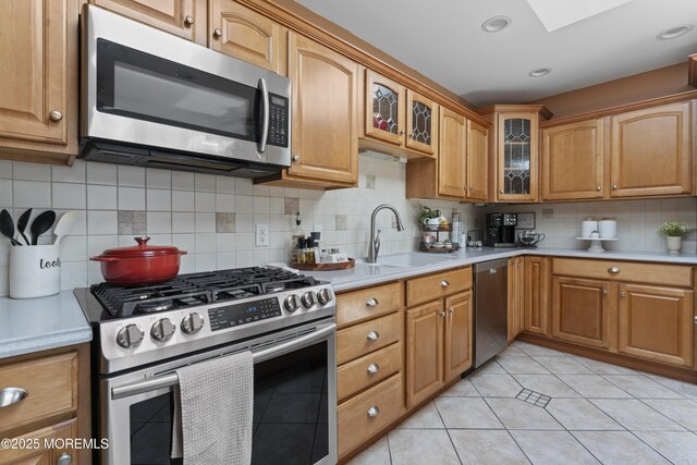 kitchen featuring a sink, light countertops, stainless steel appliances, backsplash, and glass insert cabinets