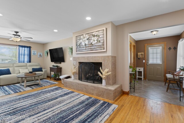 living area with a ceiling fan, a tiled fireplace, baseboards, recessed lighting, and light wood-style flooring