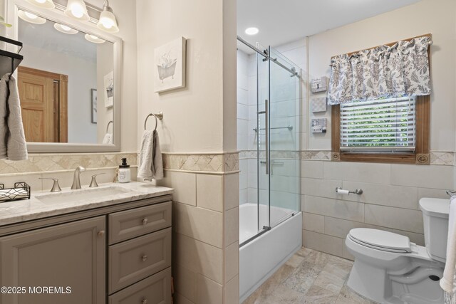 full bathroom featuring vanity, toilet, tile walls, a wainscoted wall, and enclosed tub / shower combo