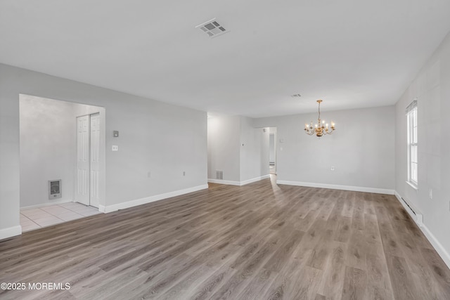 unfurnished room featuring an inviting chandelier, light wood-style floors, baseboards, a baseboard radiator, and visible vents