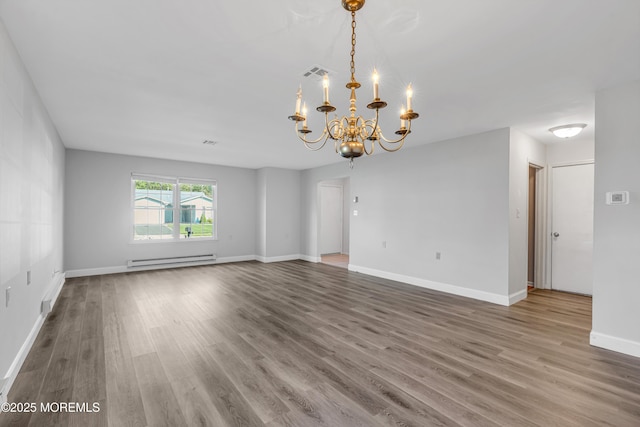 spare room featuring visible vents, wood finished floors, baseboards, a baseboard heating unit, and a chandelier