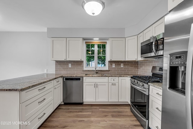 kitchen with white cabinets, light stone countertops, a sink, stainless steel appliances, and a peninsula