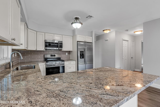 kitchen featuring light stone countertops, appliances with stainless steel finishes, a sink, a peninsula, and backsplash