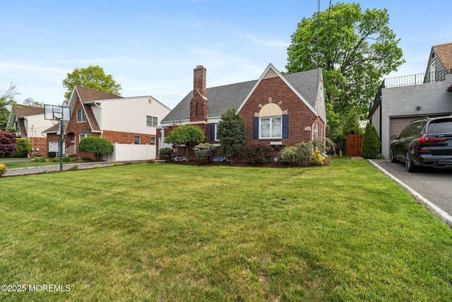 tudor home with fence, a chimney, a front lawn, and brick siding