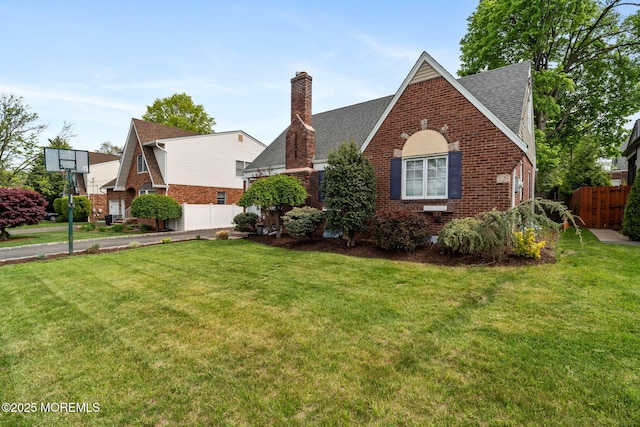 tudor-style house featuring brick siding, fence, a front yard, and a chimney