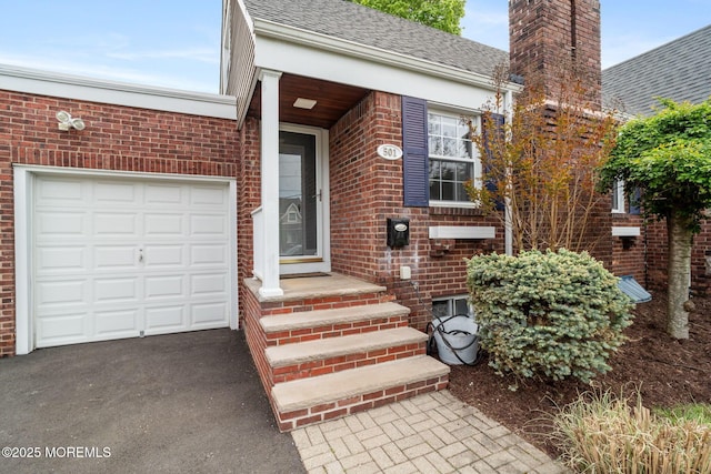 property entrance featuring a chimney, roof with shingles, a garage, brick siding, and aphalt driveway