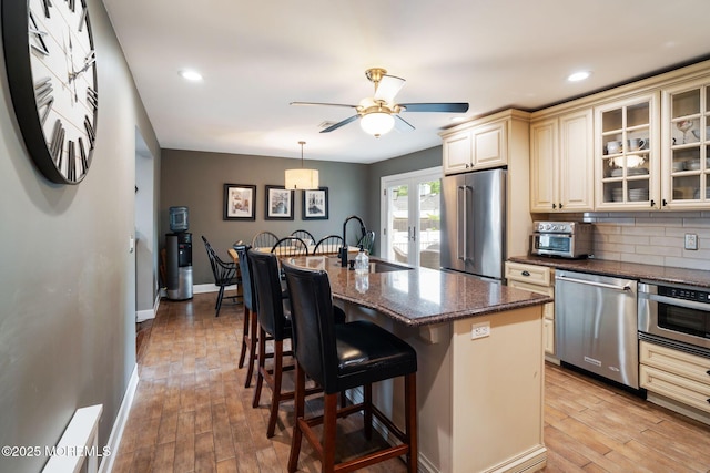 kitchen with cream cabinets, appliances with stainless steel finishes, a sink, a kitchen breakfast bar, and dark stone counters