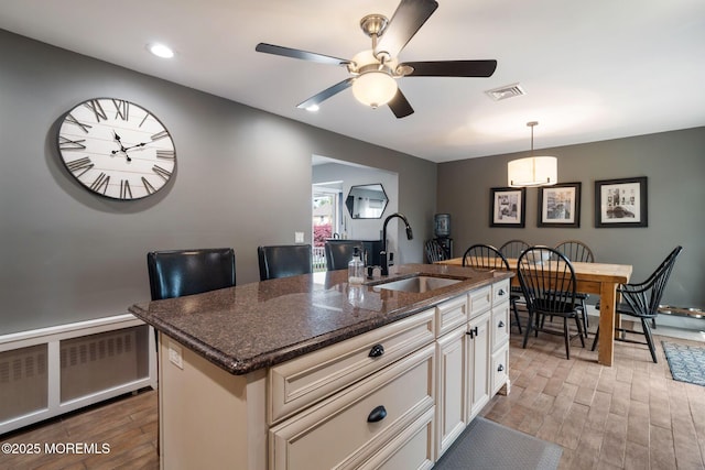 kitchen with ceiling fan, a kitchen island with sink, visible vents, a sink, and light wood finished floors