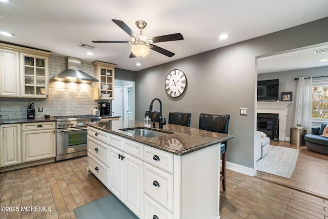 kitchen with wall chimney range hood, ceiling fan, a sink, high end stainless steel range, and light wood finished floors